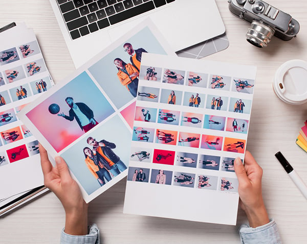 High-quality images are a must for mobile design and SEO. Hands hold photo sheets amidst laptop, camera, and coffee at a desk.