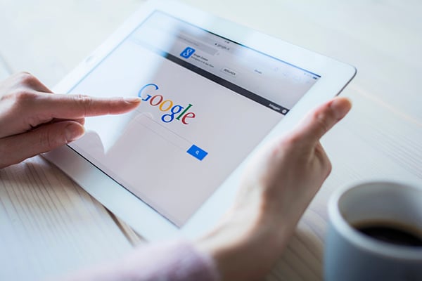 Google's algorithm affects everything about SEO. Hands holding a tablet devise displaying Google’s homepage and pointing to the Google logo on the screen.