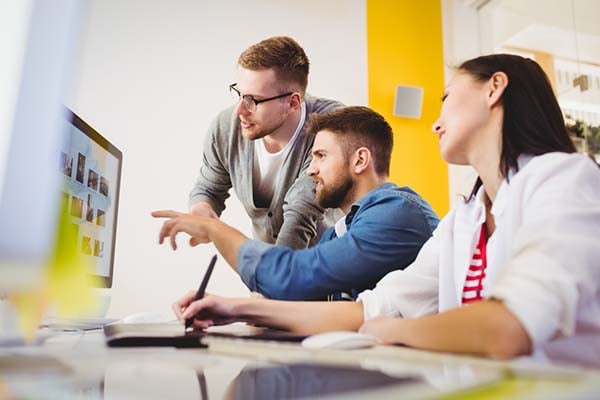 Outsourcing video for your site can be a big time saver. Three people review images on a computer screen at a desk.