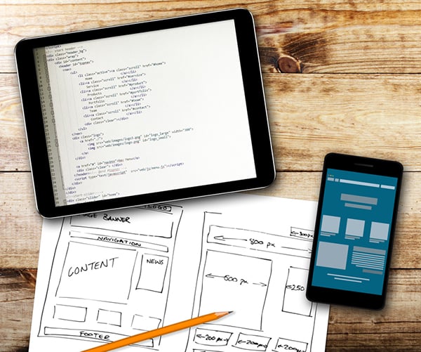 Responsive website design refers to making your site work on both desktop and mobile devices. A tablet and smartphone next paper showing a wireframe.
